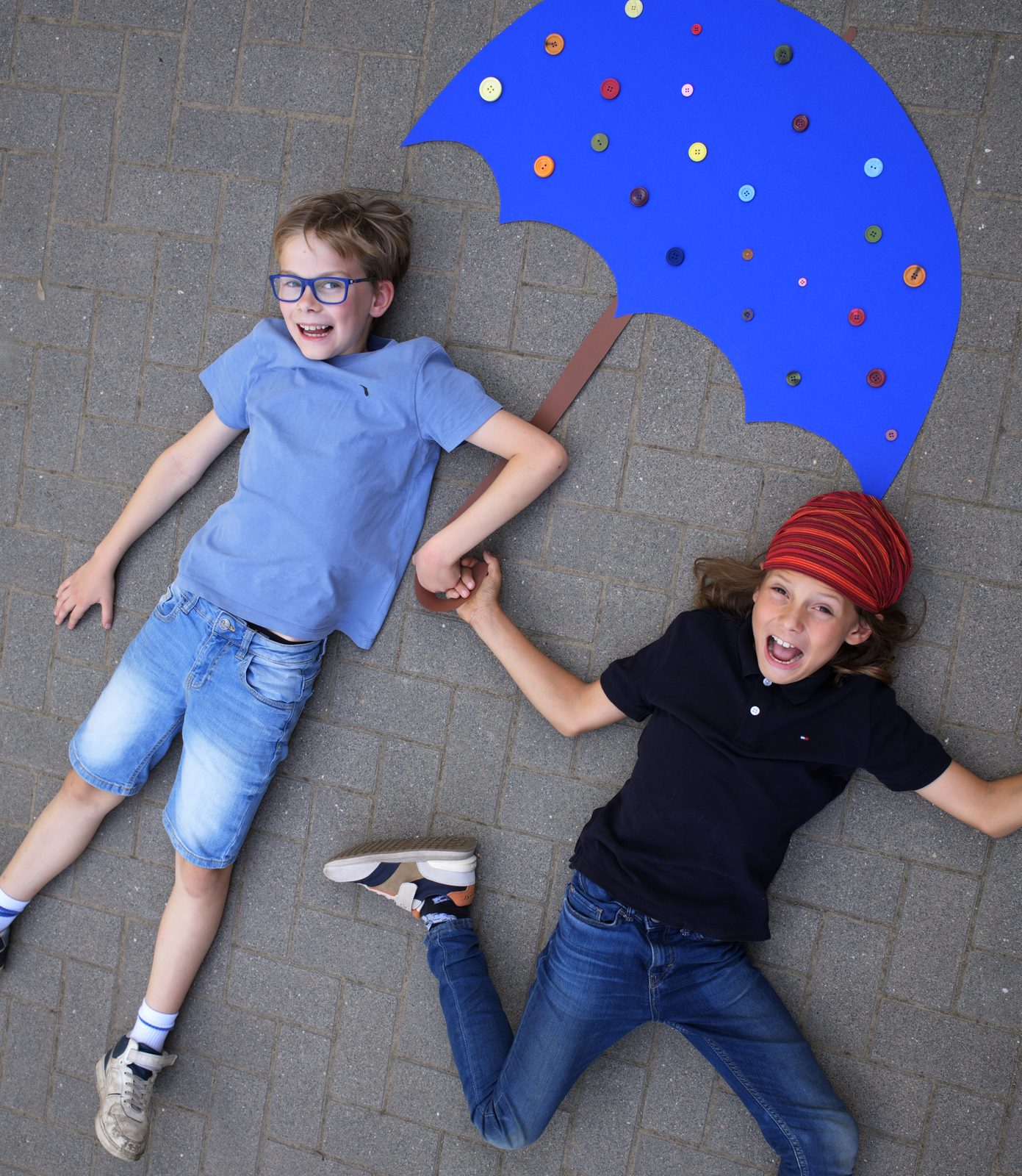 Zwei Kinder halten einen bunten Regenschirm, von oben fotografiert