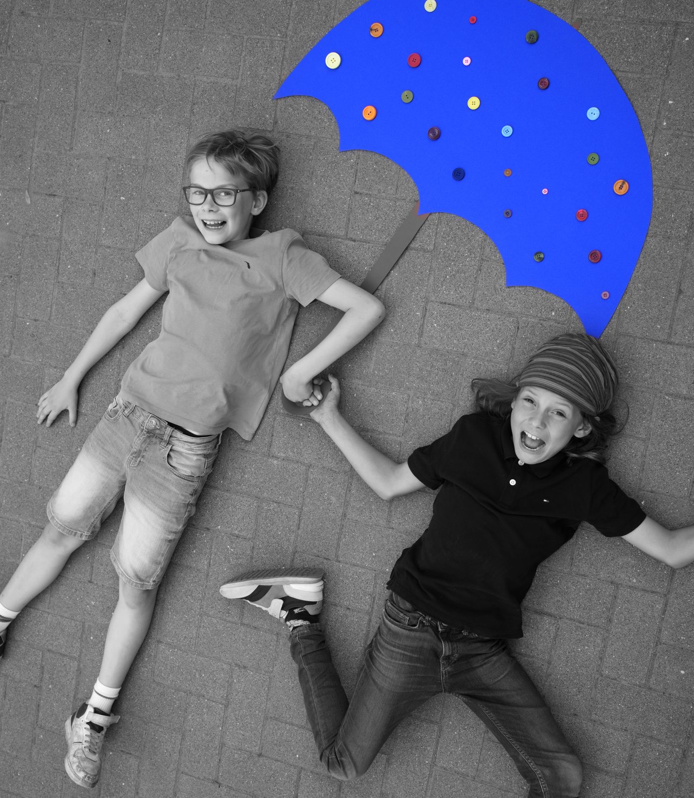 Schwarzweißfoto zweier Kinder mit buntem Regenschirm