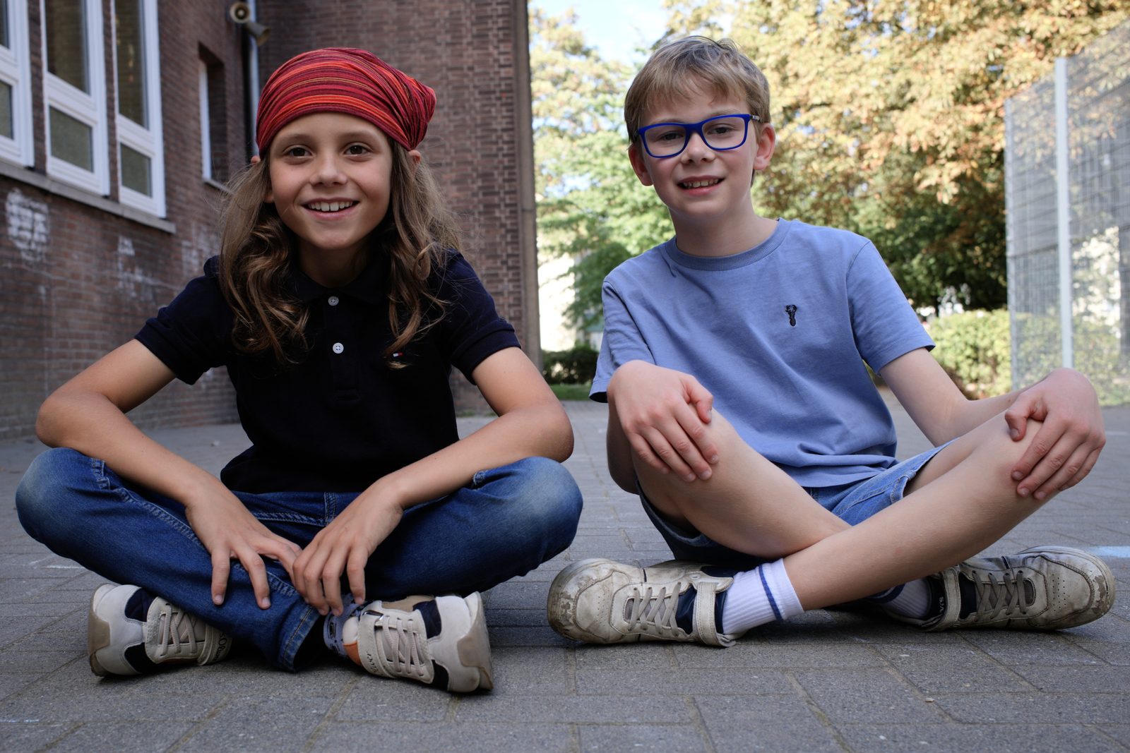 Zwei Kinder sitzen im Schneidersitz auf dem Schulhof