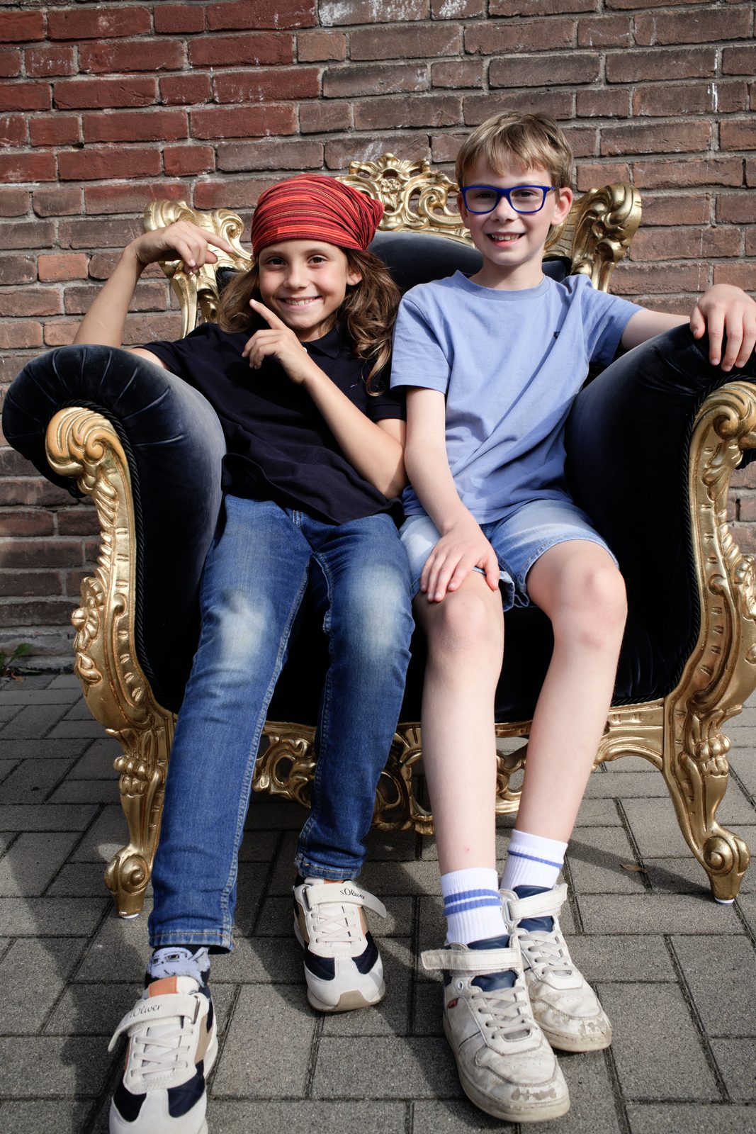 Zwei Kinder sitzen gemeinsam in einem goldverzierten Prunksessel